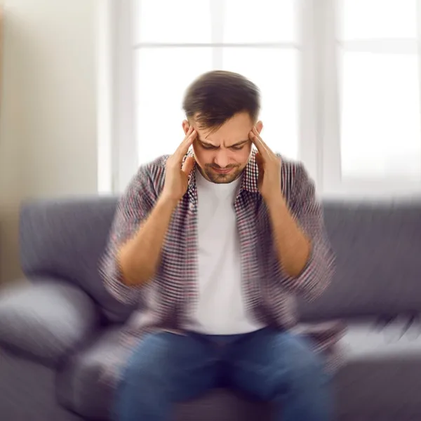 Man sitting in living room with hands over his ears because he is experiencing Diplacusis, or double-hearing.