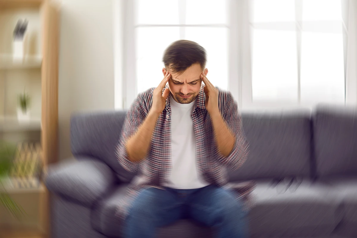 Man sitting in living room with hands over his ears because he is experiencing Diplacusis, or double-hearing.