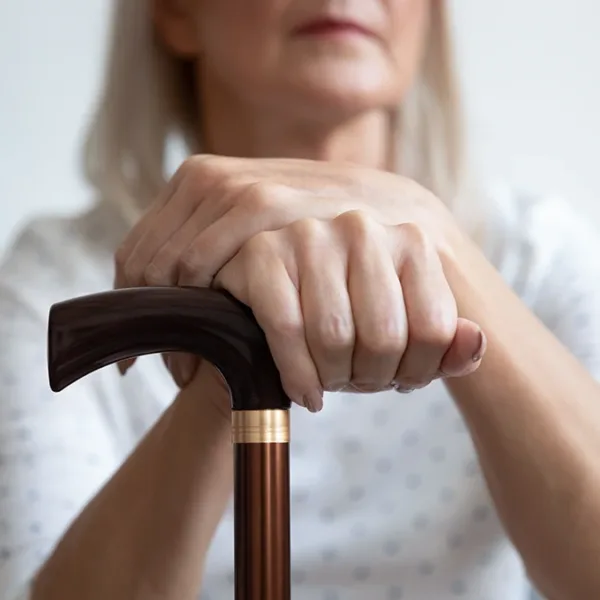 An older aged women sitting down holding a cane due to the physical effects of hearing loss causing issues with balance, dizziness, and vertigo
