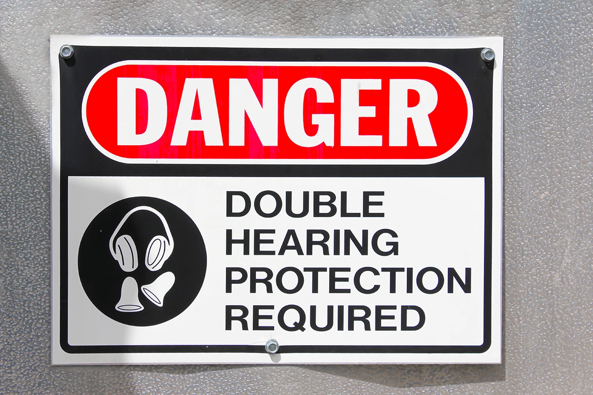 An official-looking sign hanging on a wall that reads, "Danger. Double Hearing Protection Required" in all capital letters.