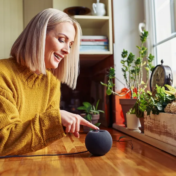 Happy mature woman connecting Alexa to hearing aids via a Bluetooth smart speaker at home in a kitchen