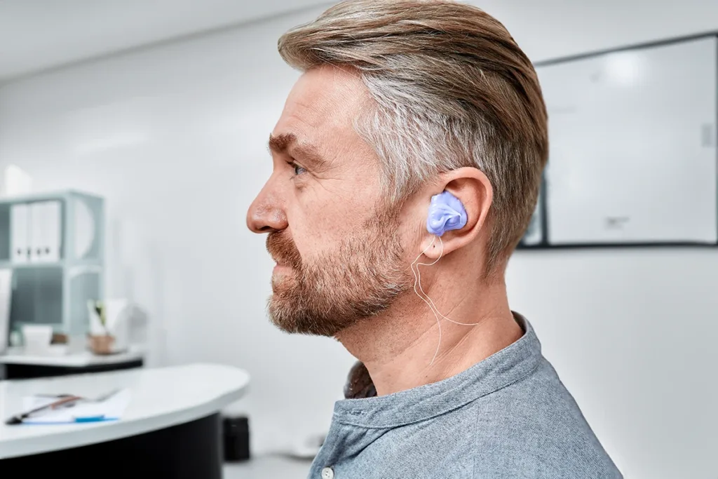 The side profile of a middle aged man, comfortably sitting in a hearing care clinic as he gets impressions of his outer ear and ear canal taken by a hearing care specialist to get custom earplugs made.