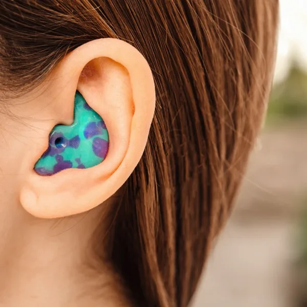 An up close view of a woman's ear wearing custom earplugs molded to the unique contours of the ears and designed to fit perfectly into the ear canal for maximum comfort and hearing protection.