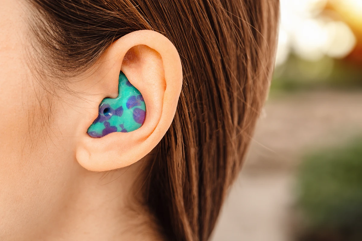 An up close view of a woman's ear wearing custom earplugs molded to the unique contours of the ears and designed to fit perfectly into the ear canal for maximum comfort and hearing protection.