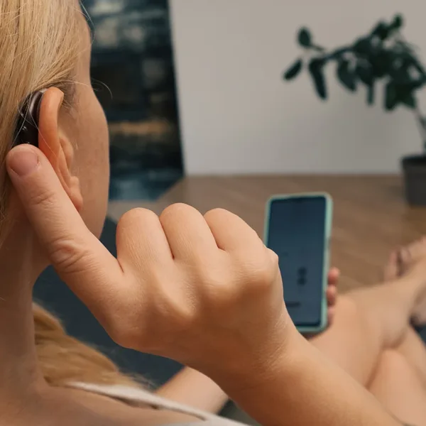 A woman wearing a BTE hearing aid and holding her smartphone using an AI Hearing Aid App.