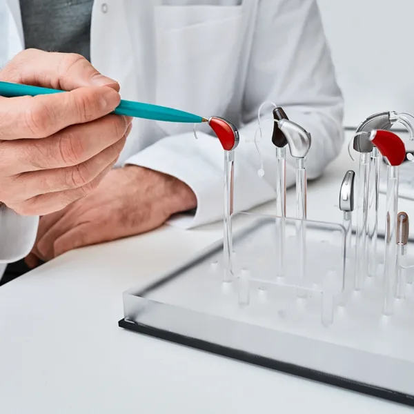 A hearing health care specialist pointing to a hearing aid displaying multiple different styles and types of hearing aids, explaining how long hearing aids last