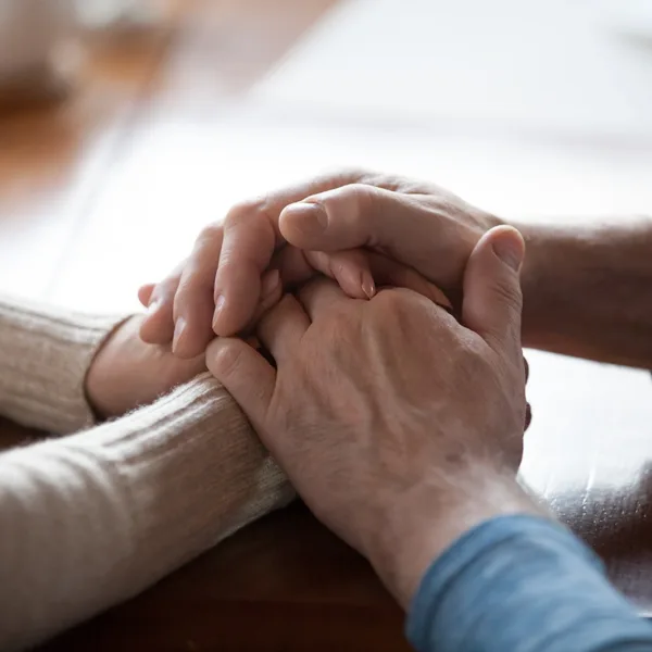 close up of senior, retirement age, older couple holding hands in a caring gesture to console one another, symbolizing how hearing loss can impact close relationships.