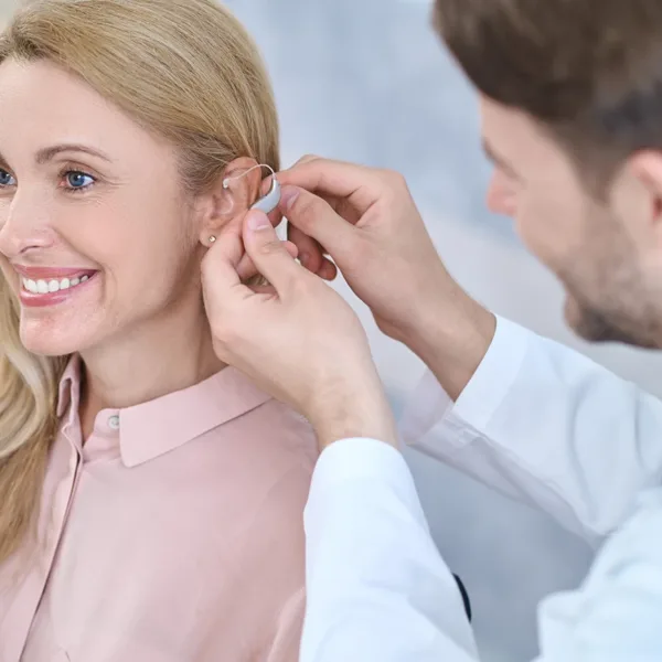 an older adult women, smiling white a hearing healthcare specialist guides her through her first hearing aid fitting appointment.