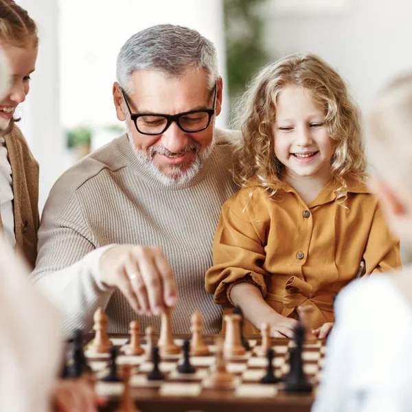 An older adult man playing chess with his grand children - AI hearing aids and cognitive brain health concept.