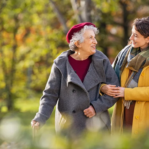 A young women and older adult women happily walking together through a beautiful outdoor park.