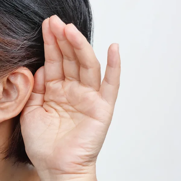 The degrees of hearing loss concept: The up close side profile of an older adult women with graying black hair, holding her hand up tp her ear trying to hearing better